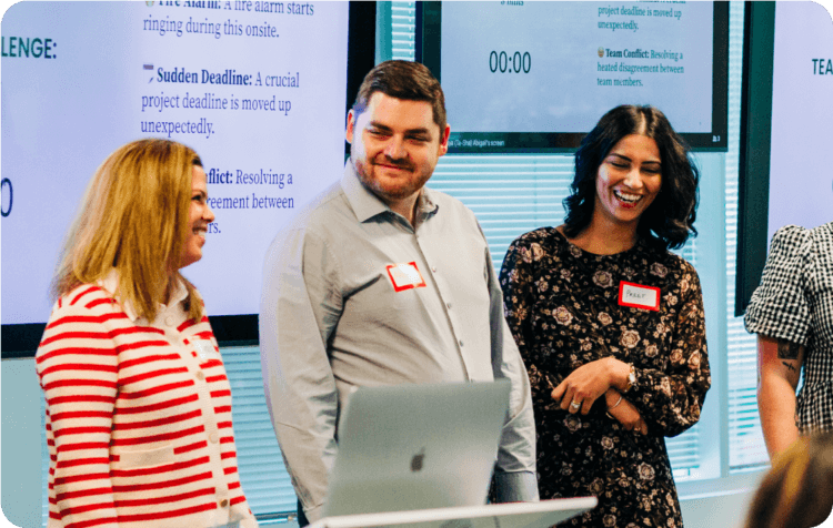 Three smiling Clio employees collaborate around a laptop during a team workshop.