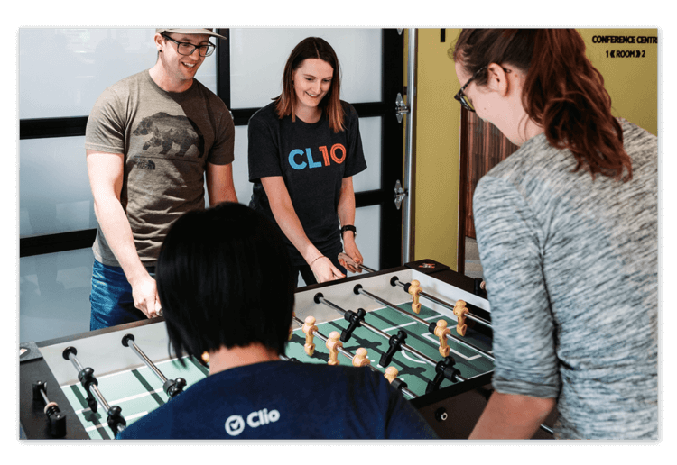 Clio teammates smile and connect while playing a game of foosball in the office lounge.
