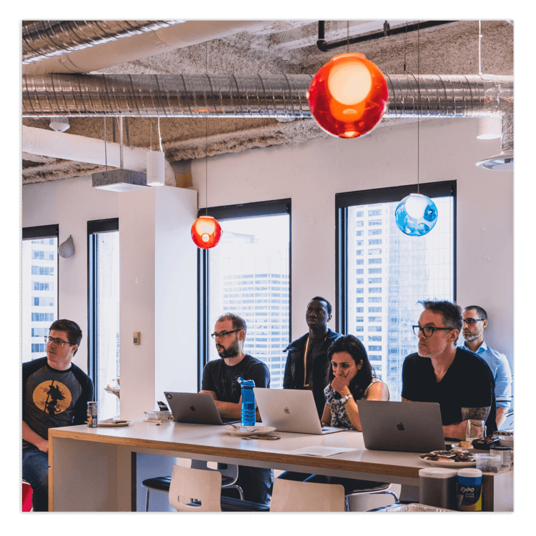 A team of Clio employees collaborates with laptops in a modern, sunlit office meeting.
