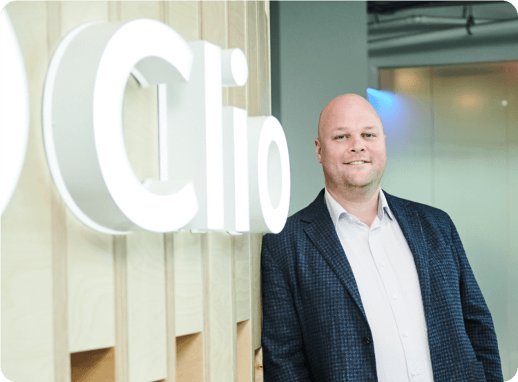 Clio CEO Jack Newton smiling while leaning against a wall with the company logo.