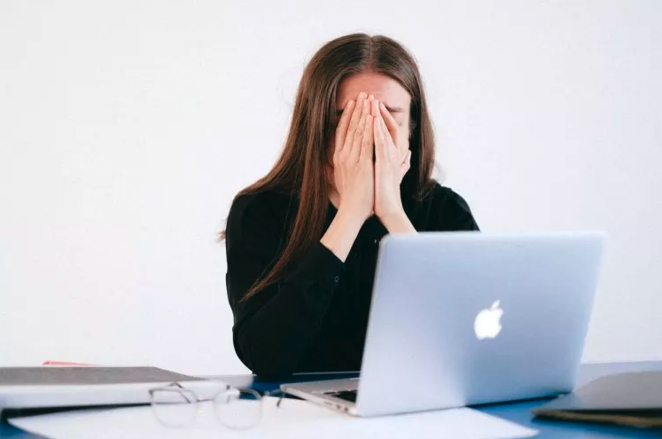 A lawyer at her laptop with her hands over her face in exhaustion from long hours.