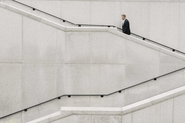 A man in a suit climbs a winding cement staircase.