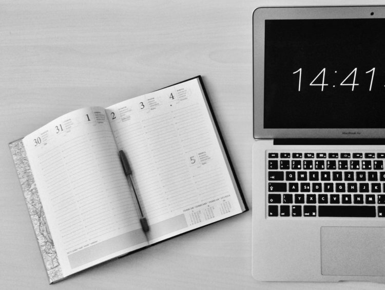 A laptop displaying the time and a planner journal lays next to it