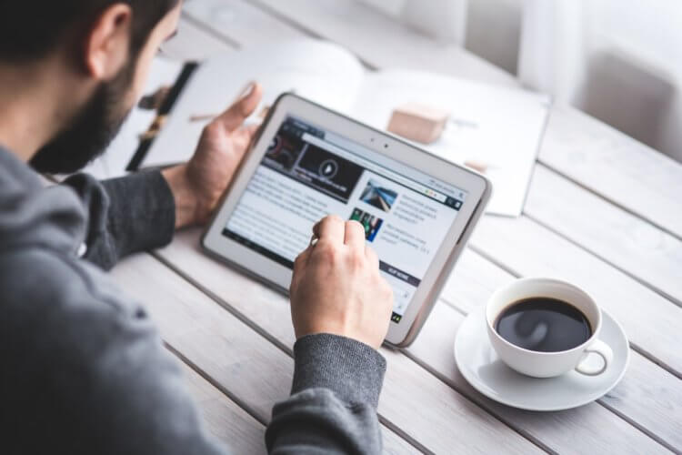 person scrolling through a website with a cup of coffee on the table