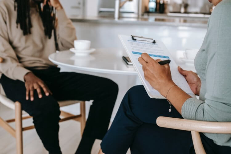 A photo of two legal professionals sitting at a table in an interview setting; one is holding a clipboard asking paralegal interview questions