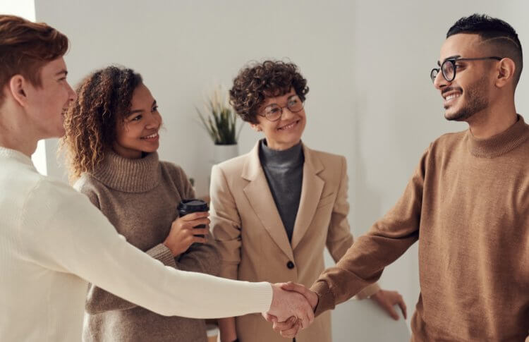 A photo of four people standing, two of whom are shaking hands