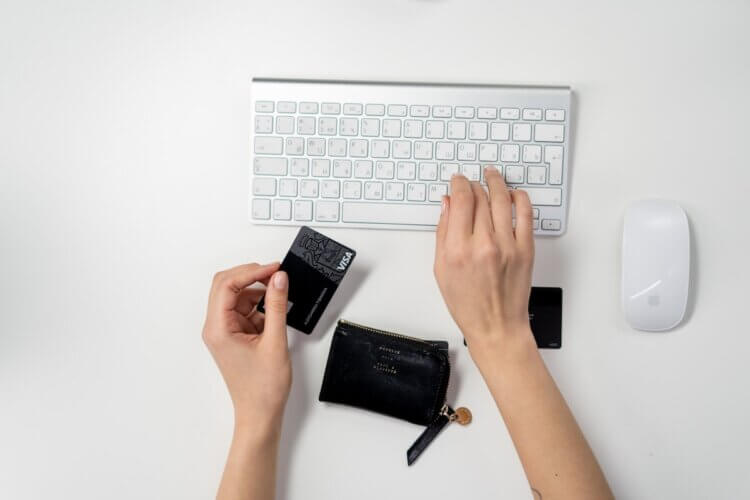 Hand holding a credit card in front of a keyboard and mouse