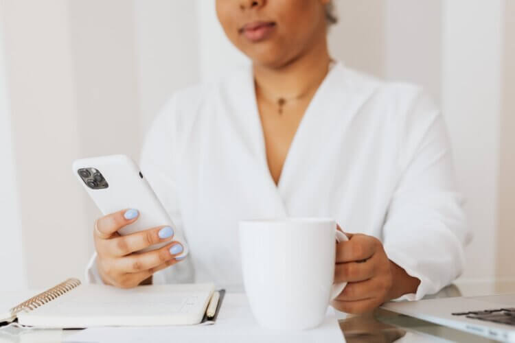 A lawyer uses Google Bard on her phone while drinking coffee at her desk.